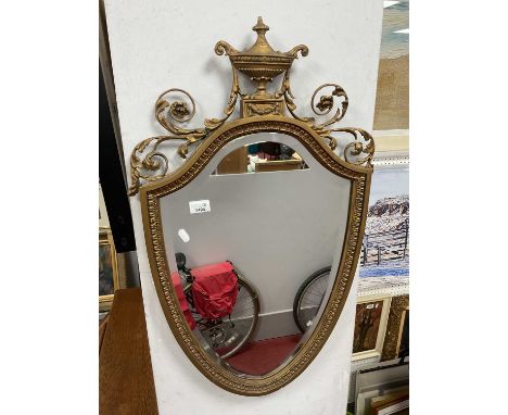 Shield-Shaped Beveled Wall Mirror, circa early XX Century in gilt wood surround with applied vase and scroll decoration atop 