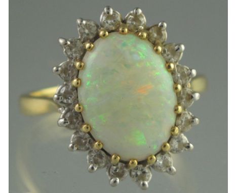 OPAL AND DIAMOND RING. The oval opal 12.5 x 9mm surrounded by eighteen diamonds. 18ct gold. Ring size R. Weight 6.1g approx.(