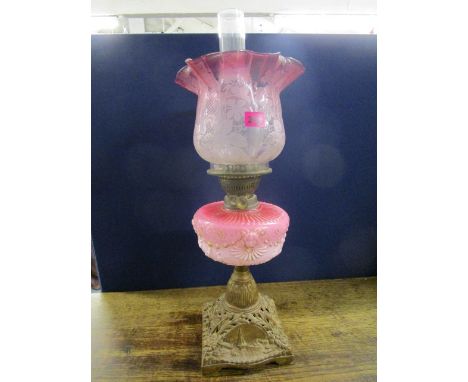 A Victorian gilt metal, brass and glass oil lamp with pink opaline reservoir decorated with a rams head and flower head swags