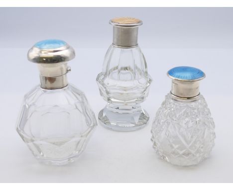 Three silver and enamel lidded glass dressing table bottles.  The largest 11 cm high. 