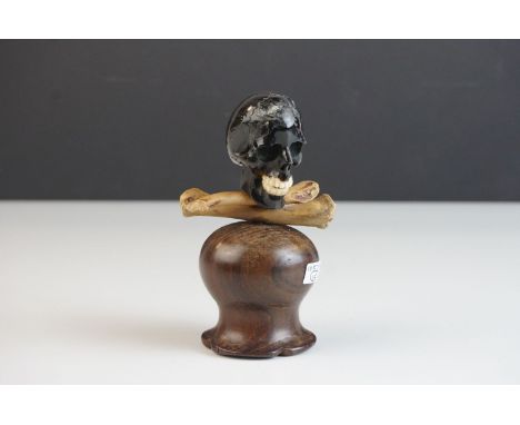 Memento Mori in the form of a Black Stone ? Carved Skull and with Wooden Carved Crossbones, raised on a turned wooden plinth,