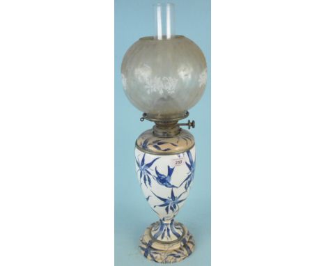 An early 20th Century ceramic based oil lamp decorated with birds, with glass shade and funnel