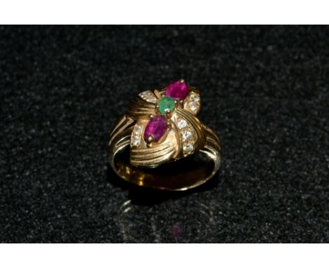 A ruby, emerald and white sapphire dress ring, tied ribbon bow crest inset wuth a central round emerald, two navette red rubi