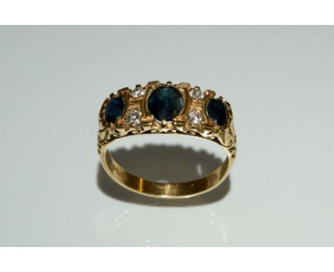 A sapphire and diamond cluster ring, inset with a central dark blue oval sapphire and two conforming smaller, each divided by