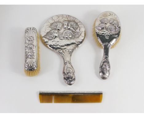 A George V silver three piece dressing table set, repousse decorated with cherub's heads, comprising hairbrush, clothes brush