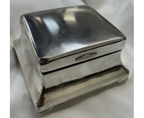 A George V silver cigarette box of square form, with an engine turned top above a waisted body on bracket feet, Birmingham, 1