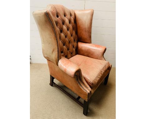 A George II style wing armchair with leather upholstered and deep button back over a loose cushion seat.