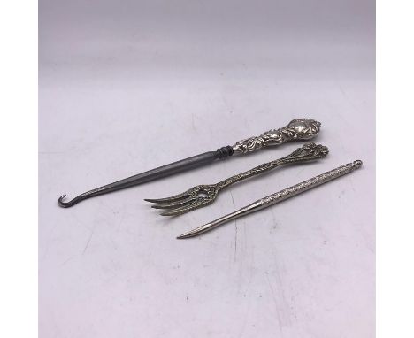 Three white metal curios to include a button hook.