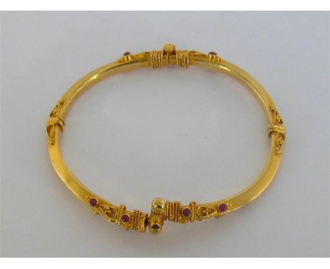A gold (tests 14 carat) and ruby hinged bangle, of Indian design, with applied wirework detail and small ruby cabochons (clas