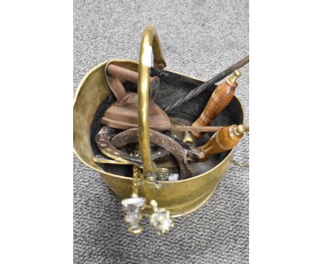 A brass coal bucket containing various fire side tools, horse shoes and a flat iron.