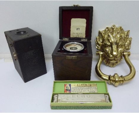 A brass lion's head door knocker, an Echo harmonica, a camera and a meter, cased