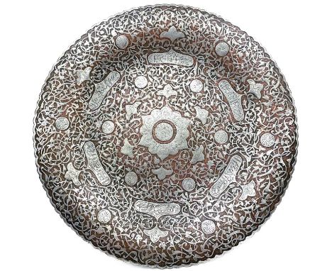 A Persian copper and inlaid silver dish, 19th century. With six shaped cartouches enclosing arabic script, diameter 26cm.From