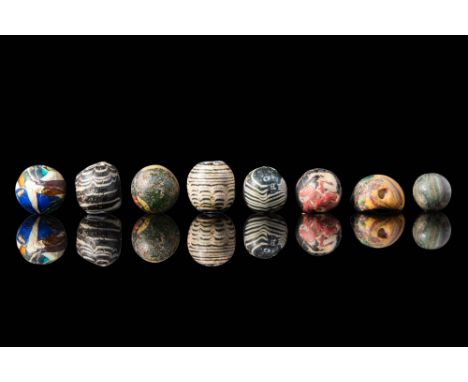 Ca. 400 BC .
A set of eight mosaic glass beads, each with a globular body. Three beads are crafted in black with white traili