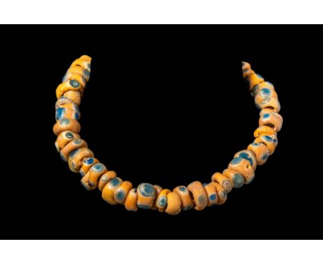 Ca. 330-70 BC.A string of glass eye beads, each annular with a large perforation for threading. The beads are opaque yellow a