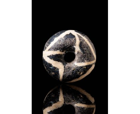 Ca. 300 - 100 BC.
A black, button-shaped bead with rounded edges, featuring a central vertical perforation. The surface is de