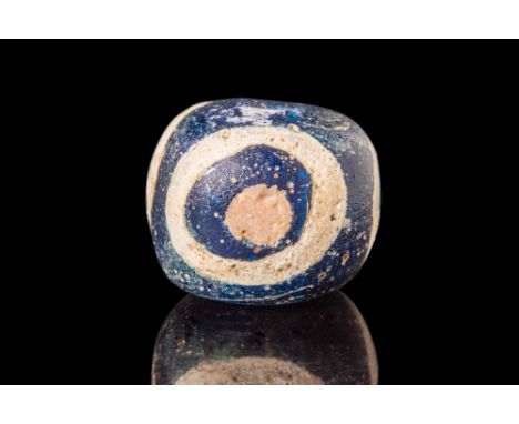 Ca. 400 BC.
A globular glass bead with a flattened upper and lower face, vertically perforated, crafted from black glass. Thr