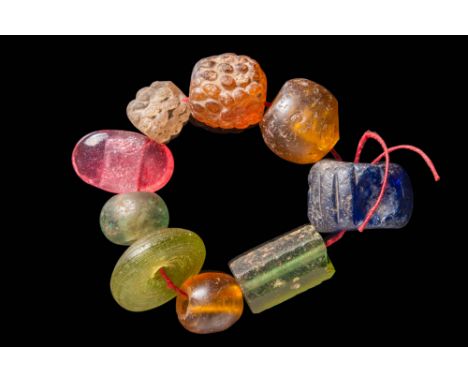 Ca. AD 100 - 300.
A group of nine translucent glass beads displaying a range of colours, including amber, pink, pale green, a