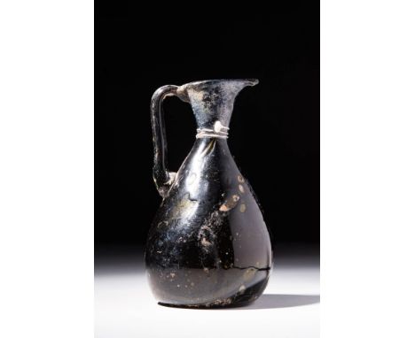 Ca. AD 700 - 800.An ewer, free-blown from translucent dark green glass. The pyriform vessel features a lengthy neck, a flared