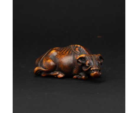 A JAPANESE BOXWOOD NETSUKE OF AN OX BY OKATOMOEDO PERIOD (1615-1868), 18TH CENTURYThe large reclining beast with the legs nea
