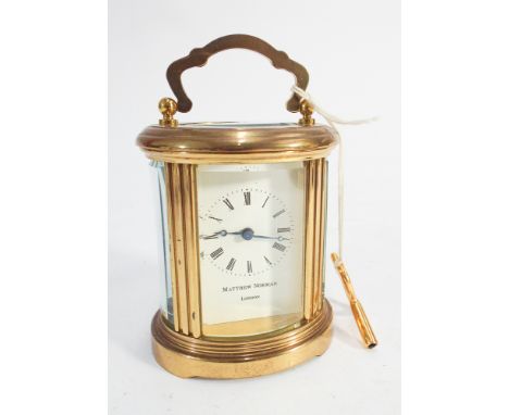 Miniature brass oval carriage clock by Mathew Norman of London.  Swiss made, 8cm high excluding handle.  With key 