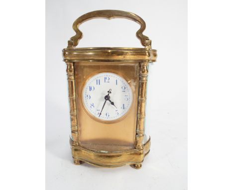 Carriage clock of shaped oval form with white enamel dial and blue numerals, with key. Height excluding handle 12cm 