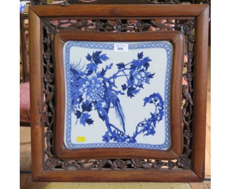 A Chinese blue and white plaque, depicting an exotic bird in flowering branches in a hardwood carved frame, 48cm square
