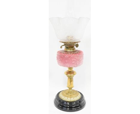 An Edwardian brass oil lamp with pink glass oil reserve to brass column and black stepped base, with an upturned floral etche