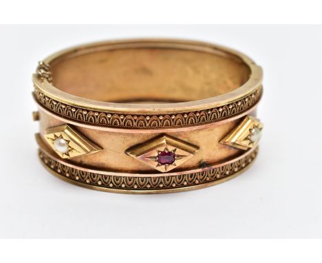A LATE VICTORIAN GEM SET HINGED BANGLE CIRCA 1890, set with a cushion shape ruby and two split pearls, within lozenge shape r