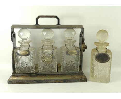 A tantalus comprising cut glass bottles and plated carrier, lacking key, with port, whisky and brandy labels, 34 by 14 by 29c