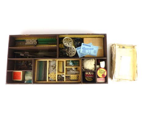 A lift top wooden storage box containing an assortment of various Meccano pieces to include wheels, nuts, tools, washers etc.