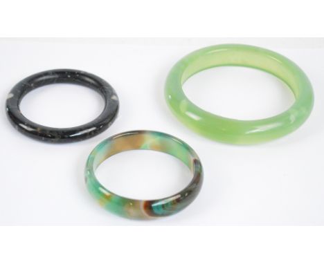 A large green hardstone bangle, diameter 11cm, and two other smaller examples including one jade, both diameter approx 8cm (3