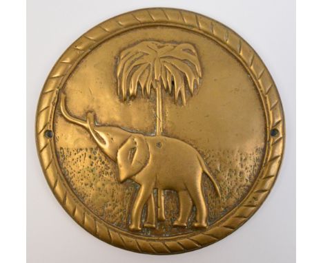 A circular brass plaque decorated with an elephant and a palm tree, reputed to be from a shipboard gun, including on HMS Anso