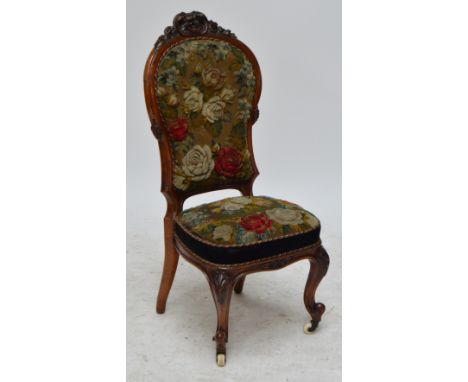 A Victorian walnut framed side chair with carved pediment above floral needlework decorated padded back and seat raised on ca