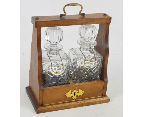 An oak tantalus housing two clear glass decanters, each with ceramic label for "Brandy" and "Whisky", width 27cm, with key.