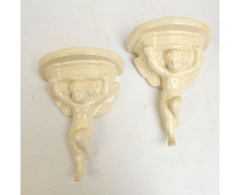 A pair of Poole ceramic wall brackets modelled as a cherub supporting a moulded cornice, height 30cm, with scratched marks an
