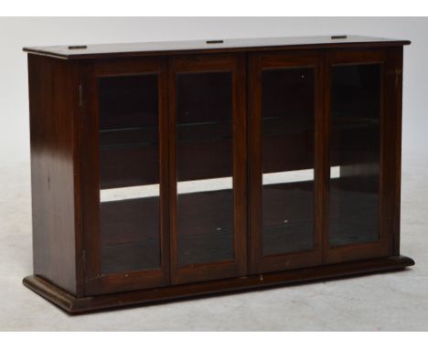 A shop style mahogany table top display cabinet with folding glazed hinged doors enclosing a glass shelf with a hinge to the 