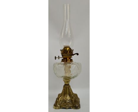 A brass oil lamp with clear glass reservoir above cast scroll decorated shaped square base, height 54cm including funnel.