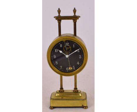 An early 20th century brass cased gravity clock, the circular glass dial set with Arabic numerals above two hexagonal turned 