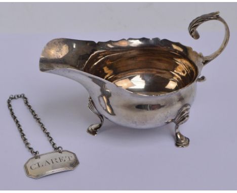 A George V hallmarked silver sauce boat with shaped rim and leaf capped C-scroll handle, raised on three outswept legs with s