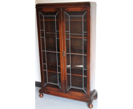 A mid 20thC oak bookcase, the caddy top raised above a pair of lead glass panelled doors hinging to reveal a fitted interior 