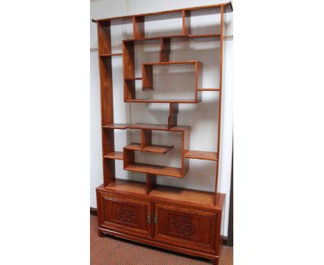 A Chinese hardwood display cabinet or open whatnot, the scroll top raised above an arrangement of pigeon holes, on a block ba