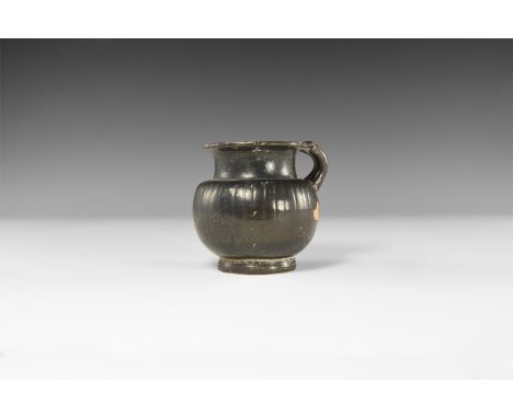 5th-3rd century AD. A ceramic blackware vessel with broad neck and narrow flared rim, collar to the neck, tall looped strap h