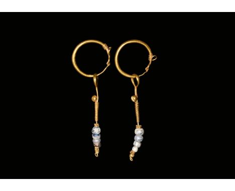 2nd century AD. A matched pair of gold earrings, each a hollow-formed ring with the ends coiled around the shank, dangle with