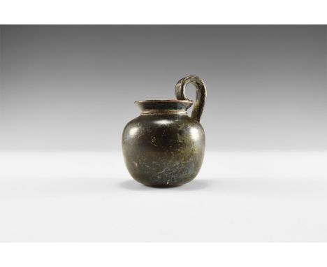 5th-3rd century BC. A squat blackware ceramic vessel with collar beneath the flared rim, tall flat-section handle to the rear