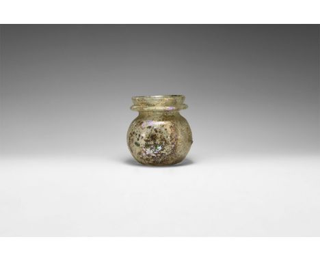 3rd-4th century AD. An iridescent glass jar with dimple base, bulbous body flange to the neck; applied bulbs of green and iri