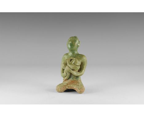 12th century AD. A green-glazed ceramic figurine of a nude seated female suckling a baby in her arms; hollow to the underside