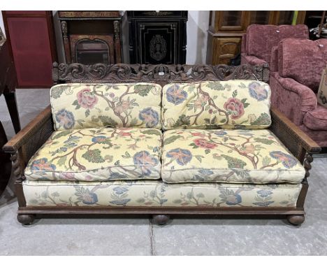 A 1930s oak carved bergere three piece sofa suite comprising a sofa (break to back) and a pair of armchairs (two caned panel 