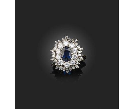 A sapphire and diamond ring, of cluster design, set with an oval sapphire, within a border of brilliant-cut and baguette diam