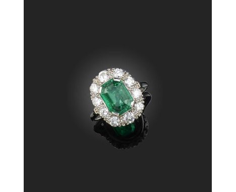 An emerald and diamond cluster ring, set with a step-cut emerald weighing approximately 2.20 carats, within a surround of rou