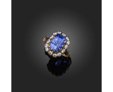 A sapphire and diamond ring, of cluster design, claw-set with a cushion-shaped sapphire weighing 8.69 carats, within a border